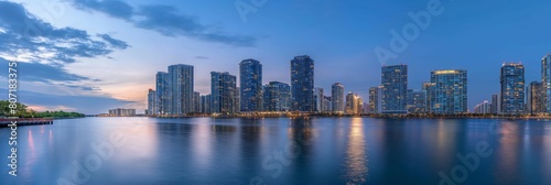 An expansive panoramic photograph of a modern city skyline reflected on water during early evening
