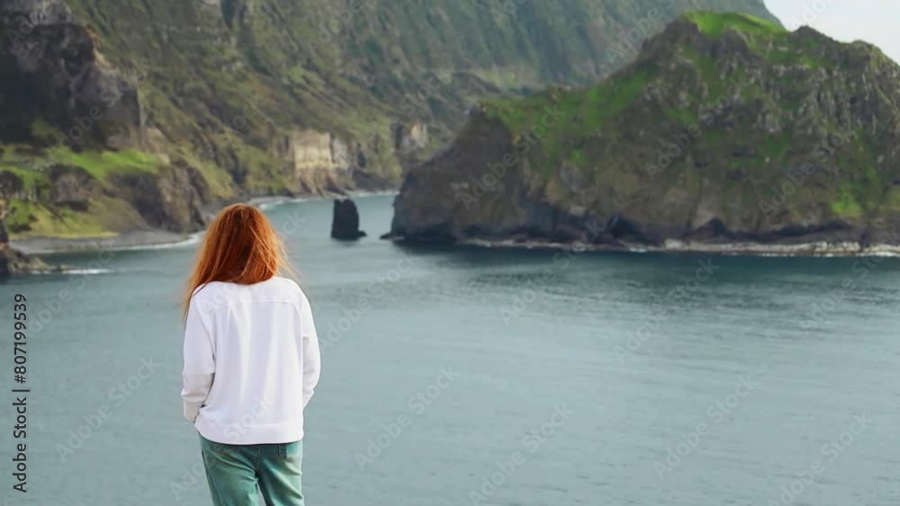 Red haired woman back view wearing jeans and white hoody observing the ocean view Arozes islands Portugal Red haired woman back view wearing jeans and white hoody observing the ocean view Arozes islands Portugal