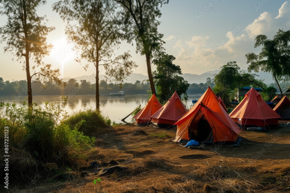 Bright tents in a tent campsite in the forest on the river bank against the backdrop of the mountains. Concept of tourism, vacation, travel, hiking
