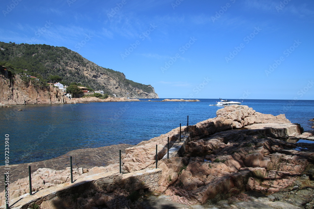 Natural and small coves of the Costa Brava with boats in the background and the blue sky with clouds and blue water. A beautiful place for vacations.