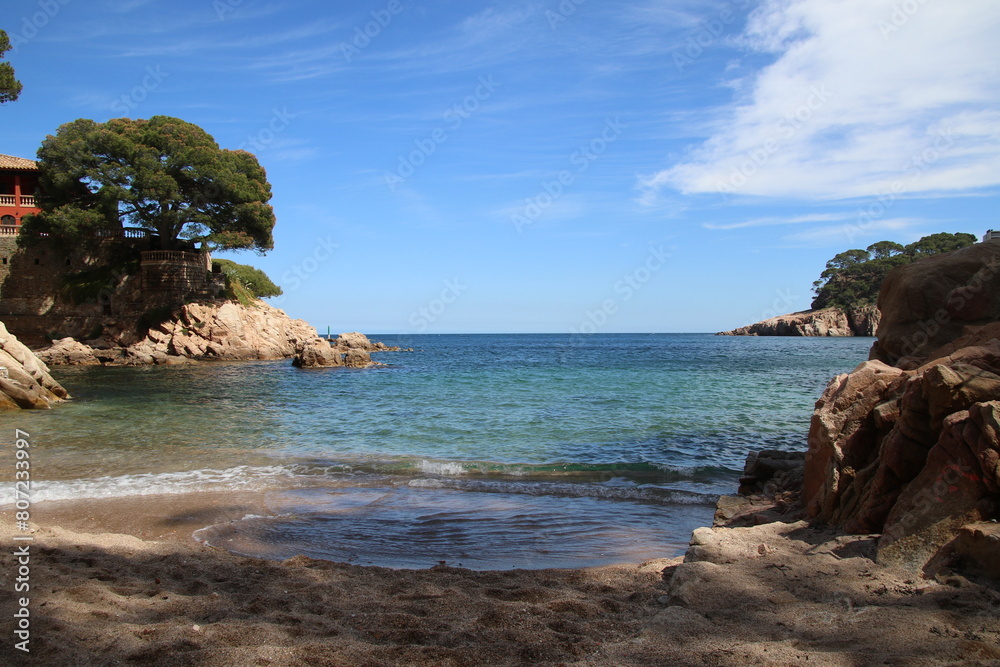 Natural and small coves of the Costa Brava with boats in the background and the blue sky with clouds and blue water. A beautiful place for vacations.