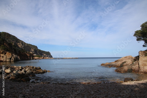 Natural and small coves of the Costa Brava with boats in the background and the blue sky with clouds and blue water. A beautiful place for vacations.
