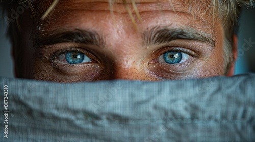   A close-up of a person with blue eyes, their face obscured by a gray blanket