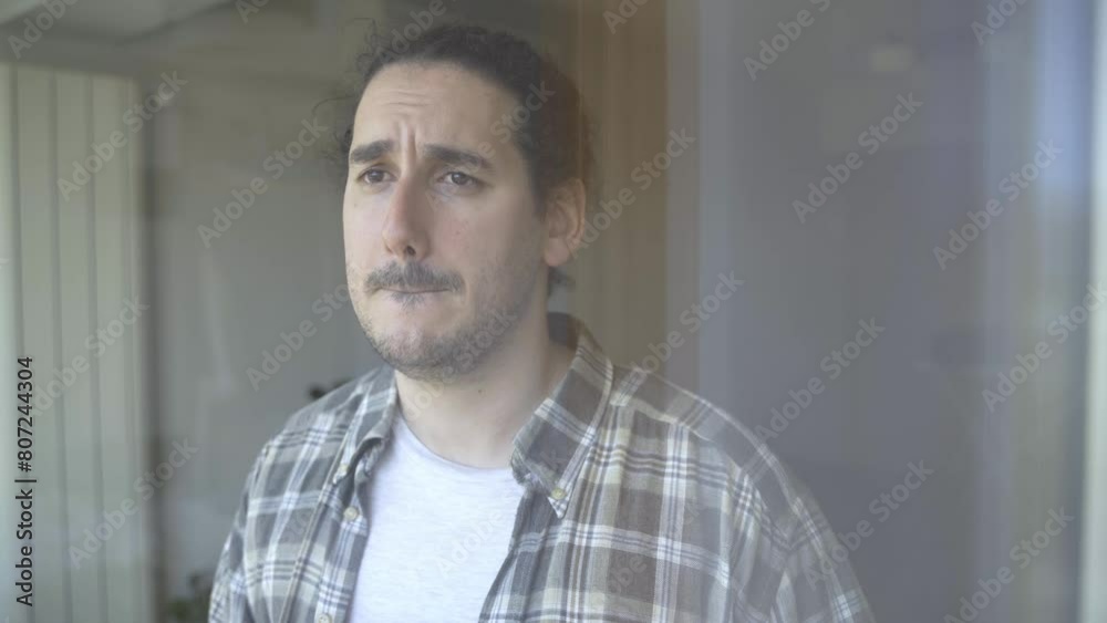 Depressed young male looks through window while drinking tea Depressed young male looks through window while drinking tea