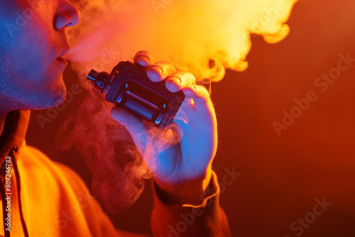 Vaping man exhales a cloud of steam, holding an electronic cigarette. Close-up.