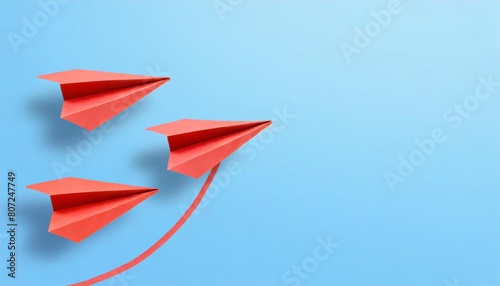 Three red paper airplanes on a light blue background, arranged in a diagonal formation with a curving trail.