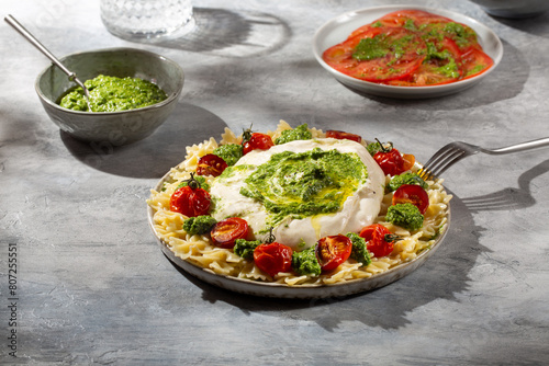 Farfalle pasta with burrata cheese, cherry tomatoes and green pesto on gray background.