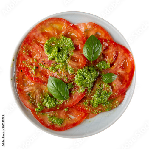 Tomato salad with green basil pesto served on gray plate isolated on white background. Top view.