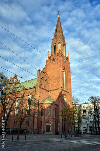 A historic, neo-Gothic Catholic church with a bell tower in the city of Poznan