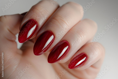 A hand holding a red manicure with a nail polish that has a shiny, glossy finish