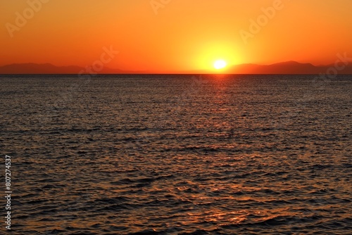 Calm dark morning sea and rising orange sun. Dawn by the sea  landscape travel photography. Distant hills over the sea and colorful sunrise.
