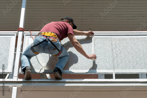A worker taping a balcony for painting. The painter hangs from safety ropes and straps.