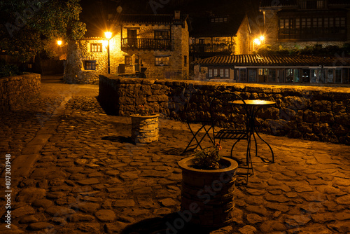 A stone walkway over the old bridge with a few tables and potted plants. The scene is quiet and peaceful at night. Barcena Mayor, Saja-Besaya Natural Park, Cantabria, Spain