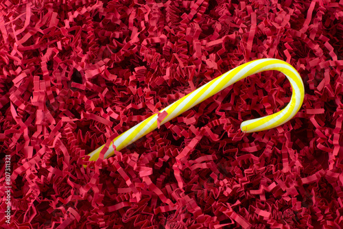 Lemon flavored yellow and white candy cane on background of crinkled shredded paper
