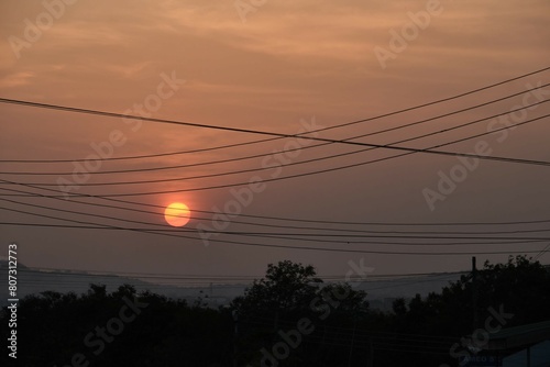 Close up view of low setting full round sun with electricity and telephone cable wires in silhouette, Accra, Ghana