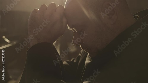 Christian monk praying with clasped hands in monastery close up. Male caucasian prayer wearing robe sitting in church during worship. Christianity concept photo