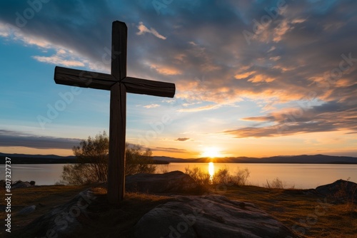 Silhouette of a cross against a dramatic sunset sky over a lake