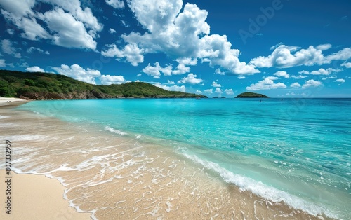 Crystal blue waters meet a pristine sandy beach under a sunny blue sky with clouds.