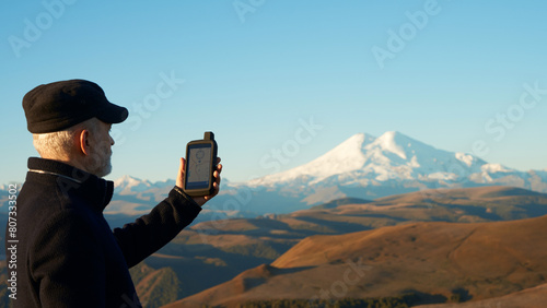 Bilde på lerret Adult man with GPS navigator in his hand on the background of mountain relief with Elbrus in the distance