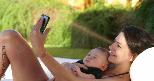 Mother taking selfie with baby son outside by the poolside © Marco