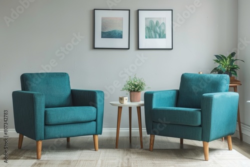 A minimalist living room with two teal armchairs positioned on either side of a small table