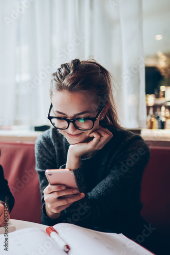 Portrait of handsome hipster guy in trendy spectacles looking at camera while sitting near female friend chatting online via mobile phone with cute smile on face at coworking space ignor talking photo