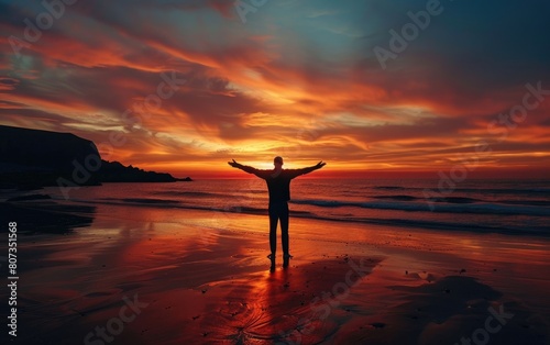 Silhouetted person with outstretched arms on a beach at sunset.