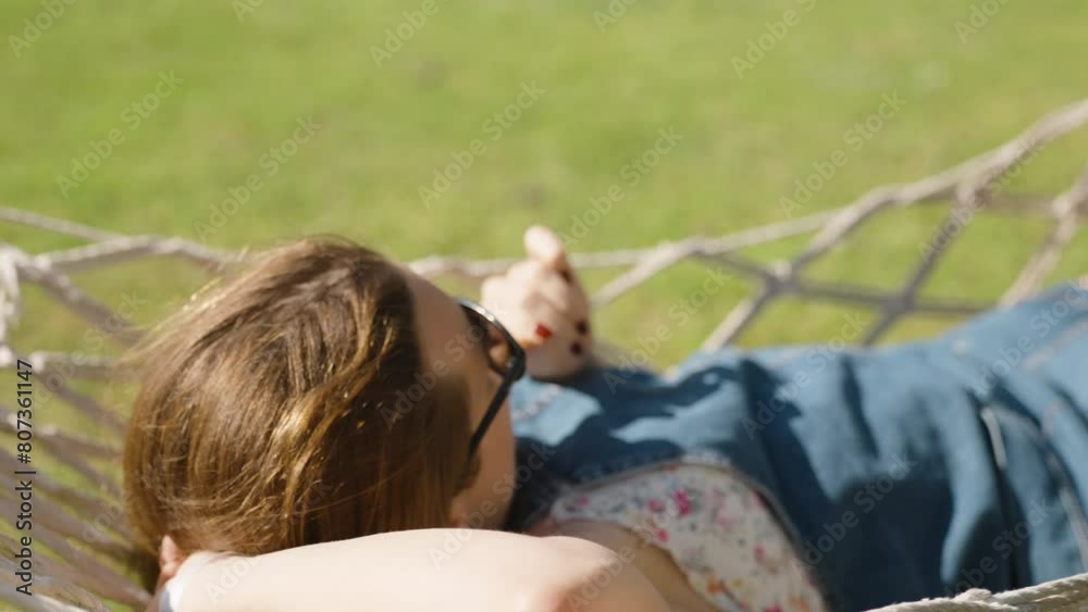 View from behind of a woman swaying in a hammock and eating ice cream under the sunlight. Carefree relaxation. View from behind of a woman swaying in a hammock and eating ice cream under the sunlight. Carefree relaxation.