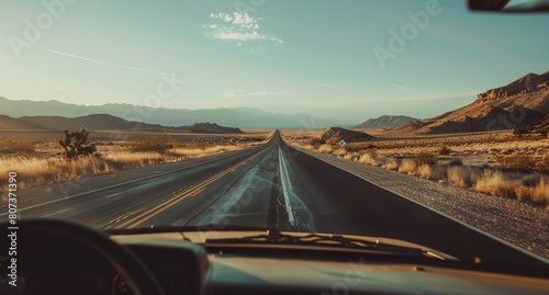 a view of a road from a vehicle in the desert with mountains in the background and a blue sky..