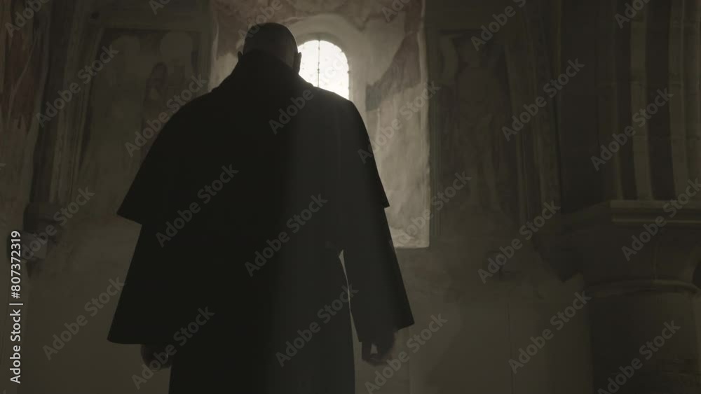 Bald Christian monk in robe silhouette standing in front of sunlit window in church back view medium shot. Religious prayer in monastery. Christianity concept Bald Christian monk in robe silhouette standing in front of sunlit window in church back view medium shot. Religious prayer in monastery. Christianity concept
