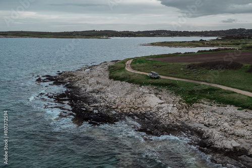 Adventure camper parked on a penninsula with rocks and wild sea. Road trip through istrian landscape. Discover istria, croatia. Gray day.