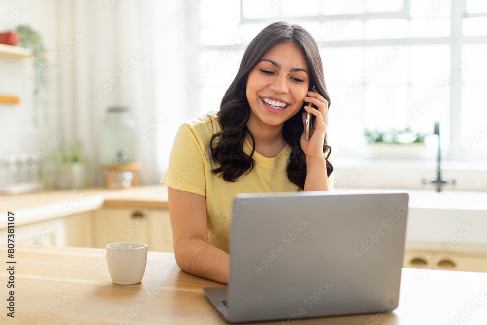 A middle eastern woman is multitasking, talking on her cell phone while working on her laptop. She appears focused and engaged in a conversation while typing on the computer. A middle eastern woman is multitasking, talking on her cell phone while working on her laptop. She appears focused and engaged in a conversation while typing on the computer.