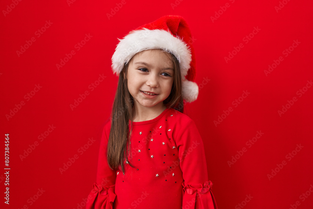 Cheerful hispanic girl donning christmas hat, a beacon of joy over red isolated background Cheerful hispanic girl donning christmas hat, a beacon of joy over red isolated background