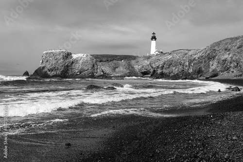 Yaquina Head Lighthouse, crashing waves, cloudy sky and black pebble beach on the central Oregon coast in classic Black and white.