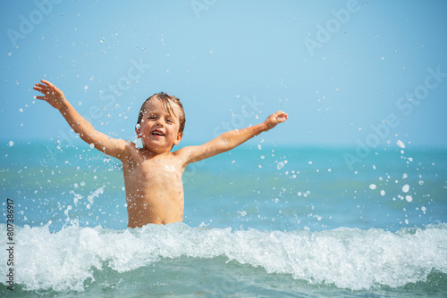 A joyful young boy with arms wide open, playing in the sea waves