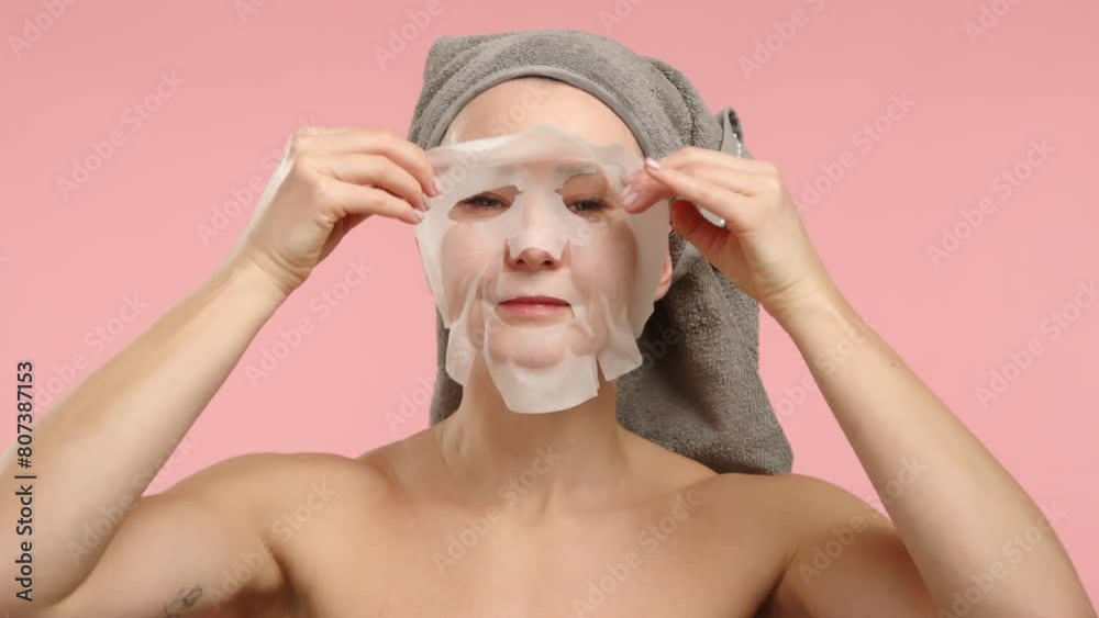 A serene scene where a woman wearing a towel turban applies a hydrating facial mask delicately, set against a soft pink backdrop to emphasize her skincare regime. A serene scene where a woman wearing a towel turban applies a hydrating facial mask delicately, set against a soft pink backdrop to emphasize her skincare regime.