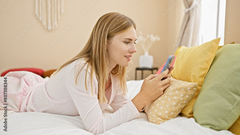 Blonde woman using smartphone in bedroom with pillows Blonde woman using smartphone in bedroom with pillows
