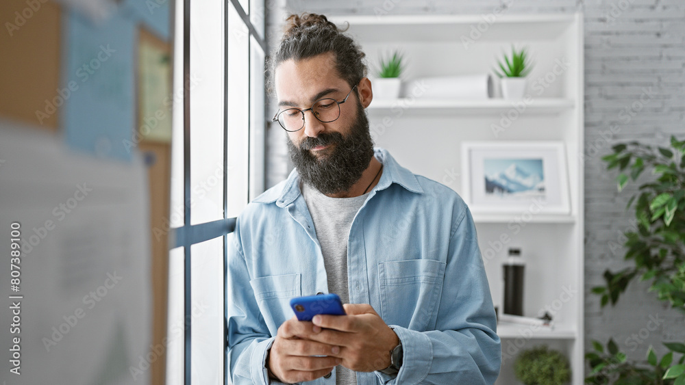 Handsome hispanic man with beard using smartphone in modern office, plants in background, embodying entrepreneur and technology. Handsome hispanic man with beard using smartphone in modern office, plants in background, embodying entrepreneur and technology.