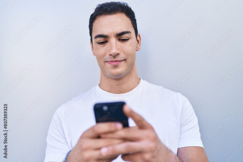Young hispanic man smiling confident using smartphone over isolated white background Young hispanic man smiling confident using smartphone over isolated white background