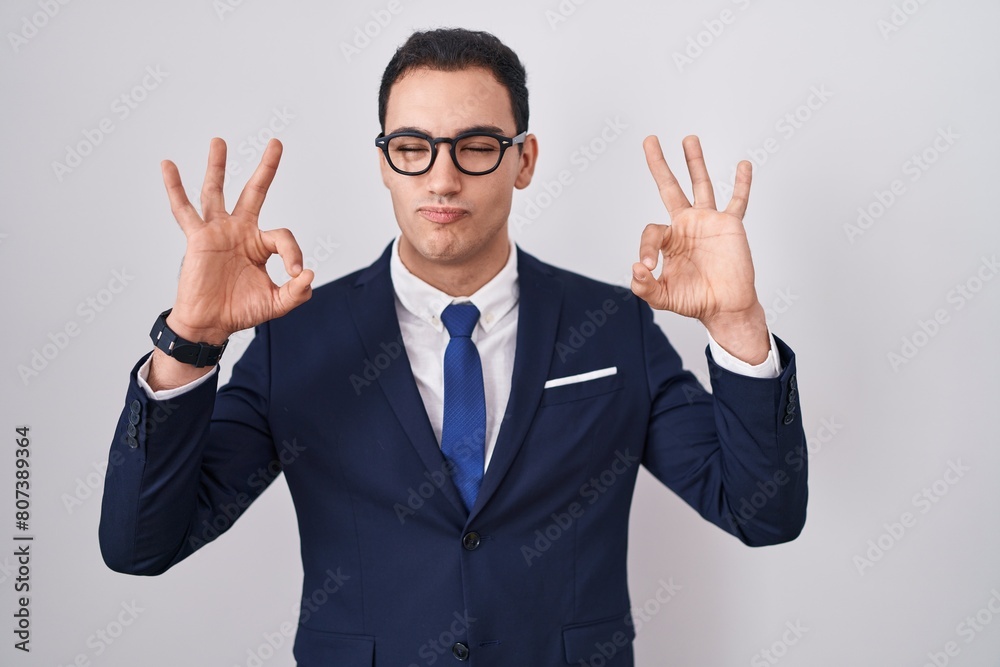 Young hispanic man wearing suit and tie relax and smiling with eyes closed doing meditation gesture with fingers. yoga concept. Young hispanic man wearing suit and tie relax and smiling with eyes closed doing meditation gesture with fingers. yoga concept.
