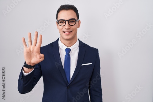 Young hispanic man wearing suit and tie showing and pointing up with fingers number four while smiling confident and happy.
