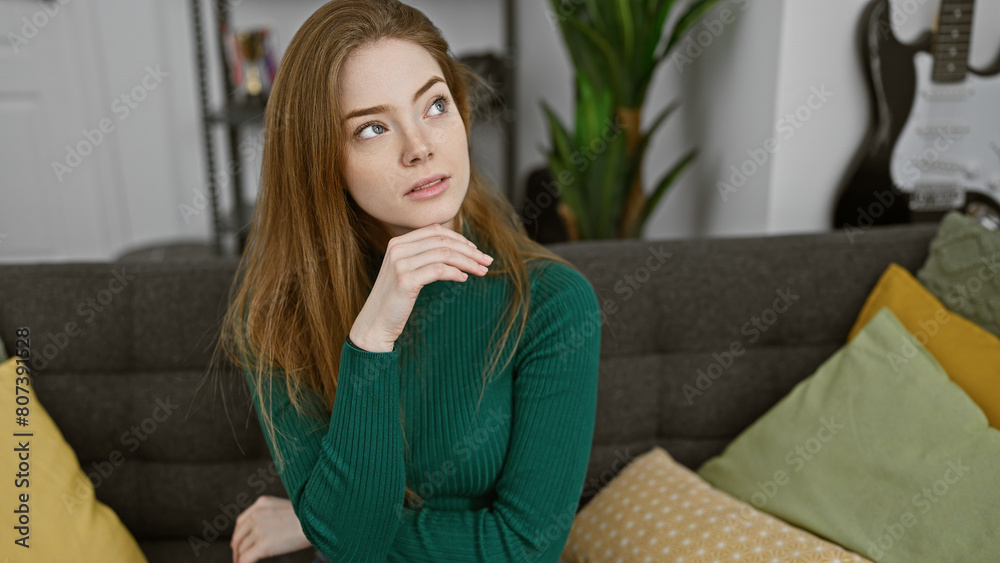 A contemplative young woman sits indoors in a cozy living room with cushions and a guitar in the background. A contemplative young woman sits indoors in a cozy living room with cushions and a guitar in the background.