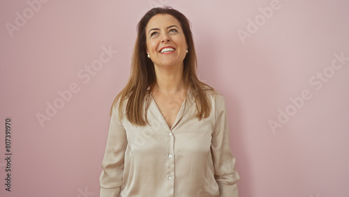 A smiling adult woman in a stylish blouse against a pink background exudes confidence and charm. photo