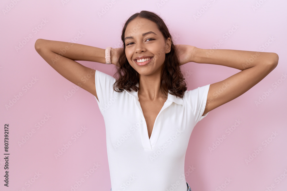 Young hispanic woman wearing casual white t shirt relaxing and stretching, arms and hands behind head and neck smiling happy Young hispanic woman wearing casual white t shirt relaxing and stretching, arms and hands behind head and neck smiling happy