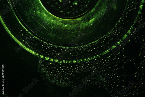 Burbujas de agua color verde sobre la superficie líquida de un cuenco de cristal transparente, con bordes liminosos en forma de arcos y curvas, produce un original diseño abstracto con fondo negro. photo