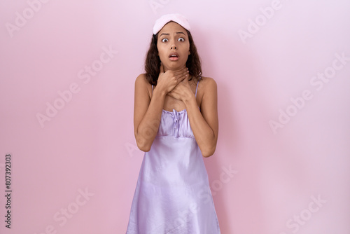 Young hispanic woman wearing sleep mask and nightgown shouting suffocate because painful strangle. health problem. asphyxiate and suicide concept.