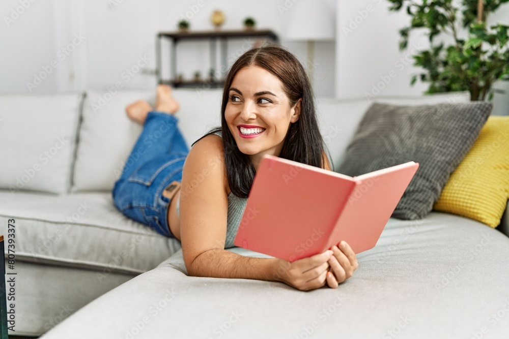 Young beautiful hispanic woman reading book lying on sofa at home Young beautiful hispanic woman reading book lying on sofa at home