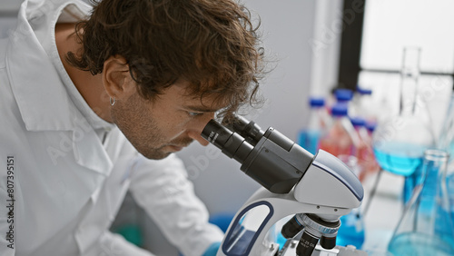 Hispanic researcher man examines samples using a microscope in a modern laboratory setting.