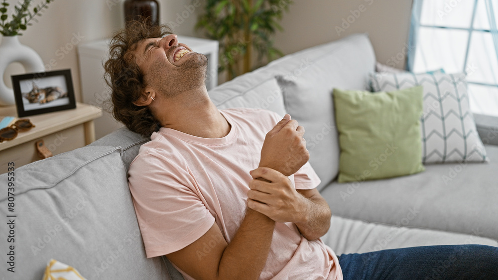 Laughing hispanic man comfortably relaxes on a sofa in a cozy living room Laughing hispanic man comfortably relaxes on a sofa in a cozy living room