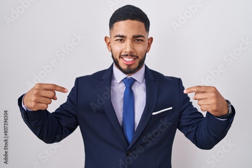 Young hispanic man wearing business suit and tie looking confident with smile on face, pointing oneself with fingers proud and happy.
